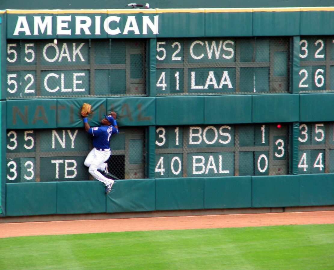 An outfielder for the Texas Rangers team attempts to catch a baseball by jumping at the wall. Ball is too high hitting just under the word American - Texas View
