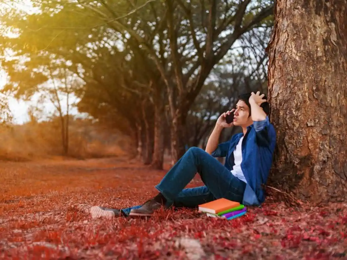 Man sat by a tree on a cell phone. - Texas View