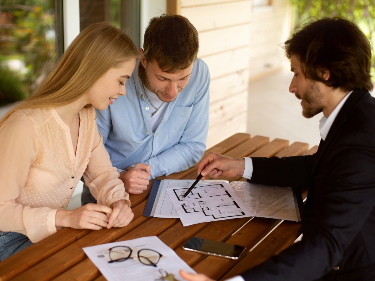 Property manager showing house plan to his clients at table on porch - Texas View