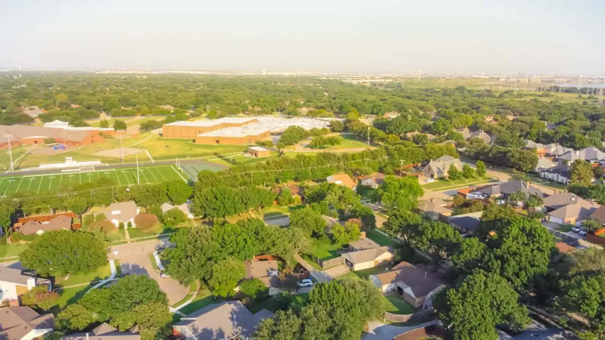 Residential neighborhood in school district with football field in background near Dallas Texas America. Suburban houses with large fenced backyard and large tree in early summer morning light. - Texas View