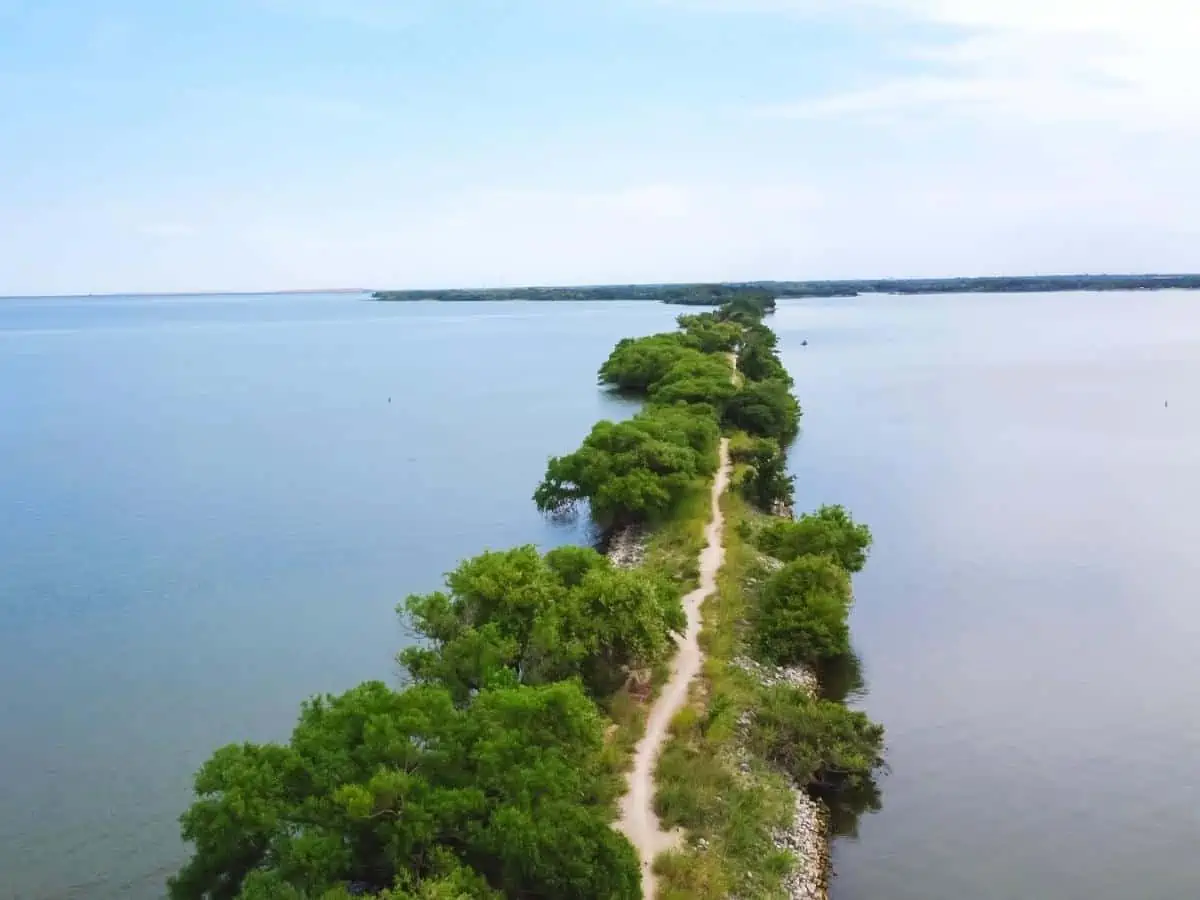 Aerial view lakeside long straight hiking trail with lush green tree lead to The Old Lake Dallas Dam from Lake Lewisville Texas America. Waterfront woody unpaved roads summertime to horizontal line. - Texas View