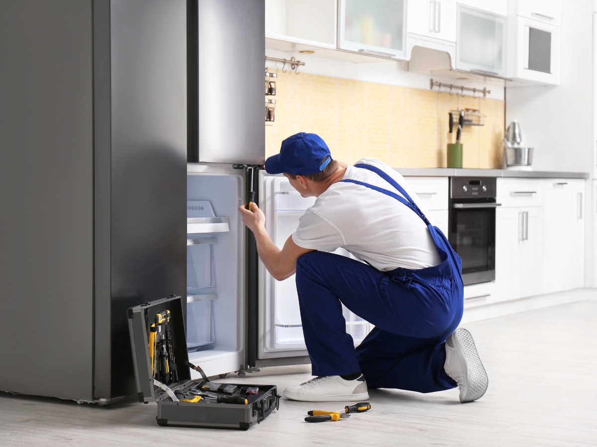Technician with Screwdriver Repairing Refrigerator in Kitchen - Texas View