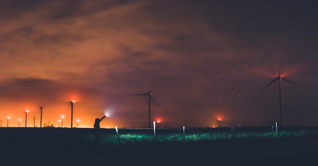 Silhouette of a person near wind turbines at night under cloudy sky in Texas.