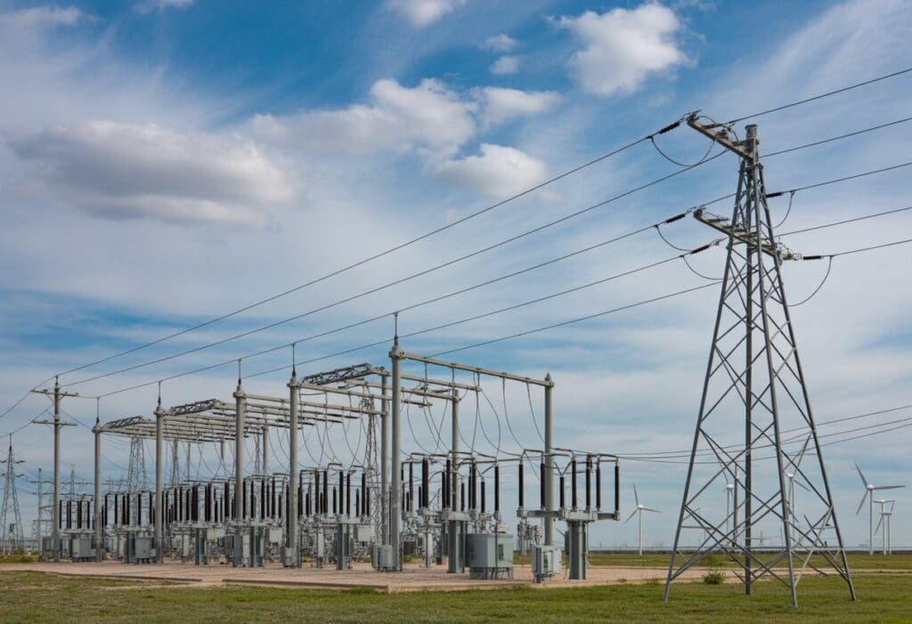 Electrical substation with power lines and transformers in a flat Texas landscape under a blue sky.