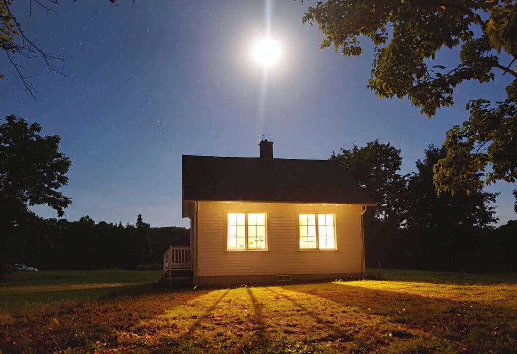 Night scene: Illuminated cottage under a bright moon. Energy-efficient lighting glows from the windows. Power, electricity.