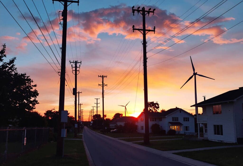 Sunset over street with power lines and wind turbine. Renewable energy, electricity.